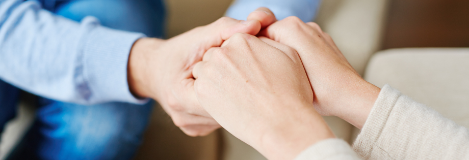 A close-up of two people gently clasping hands together, conveying comfort and compassionate support.