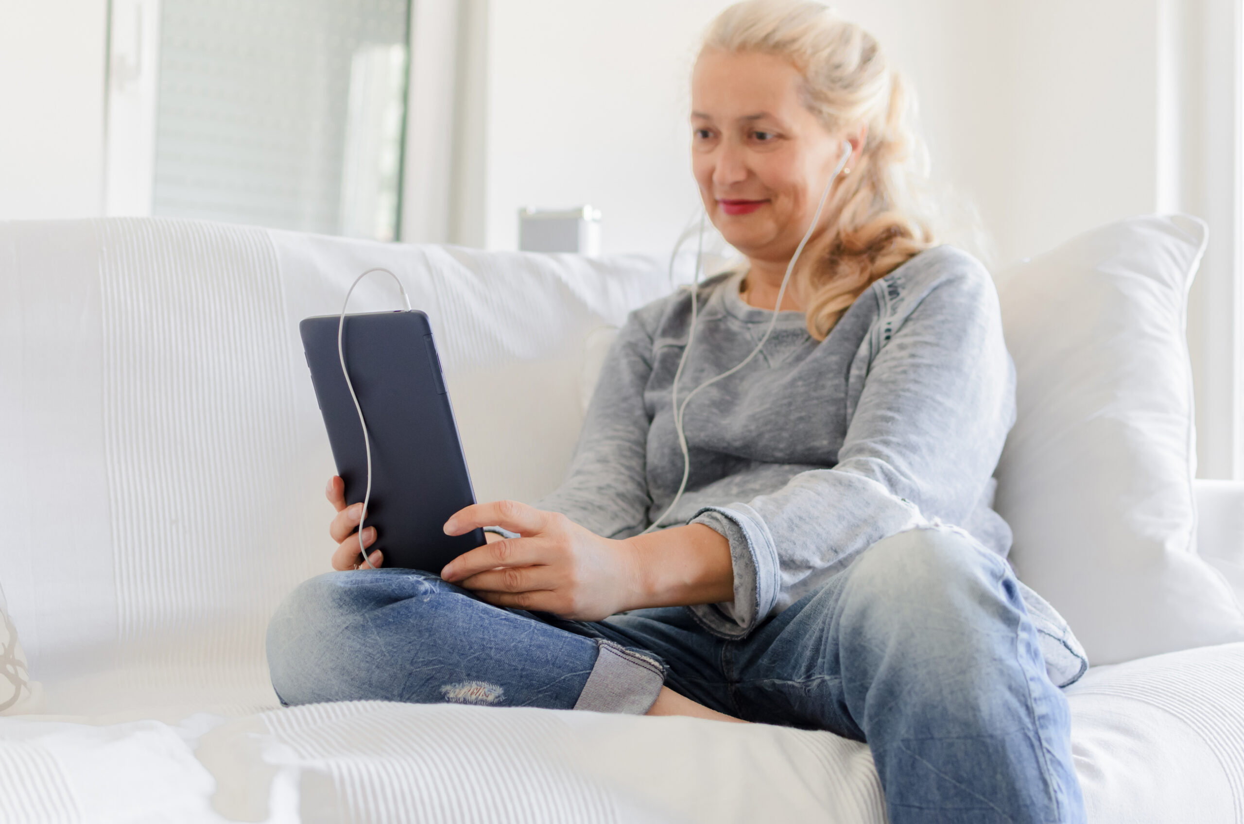 Senior woman sitting on sofa at home and looking something on tablet.