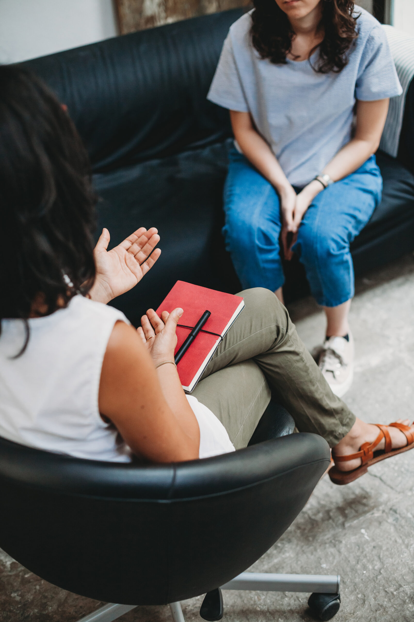 Counseling session. Professional is speaking to woman on a black couch who is listening.