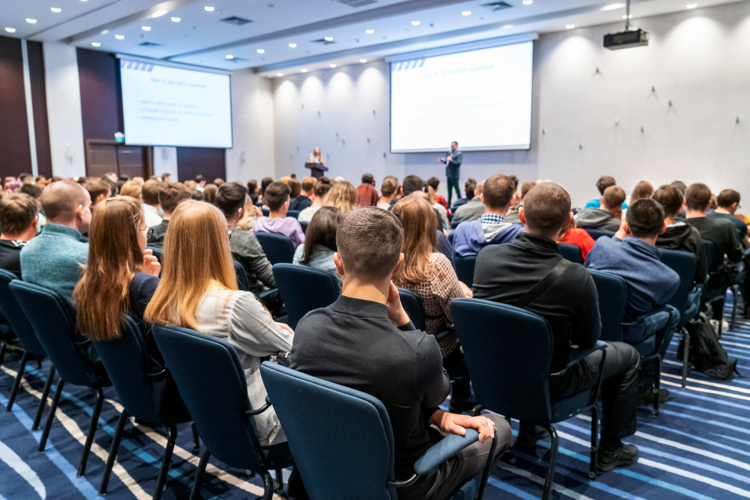 Image of large convention center room with workshop participants listening to a speaker