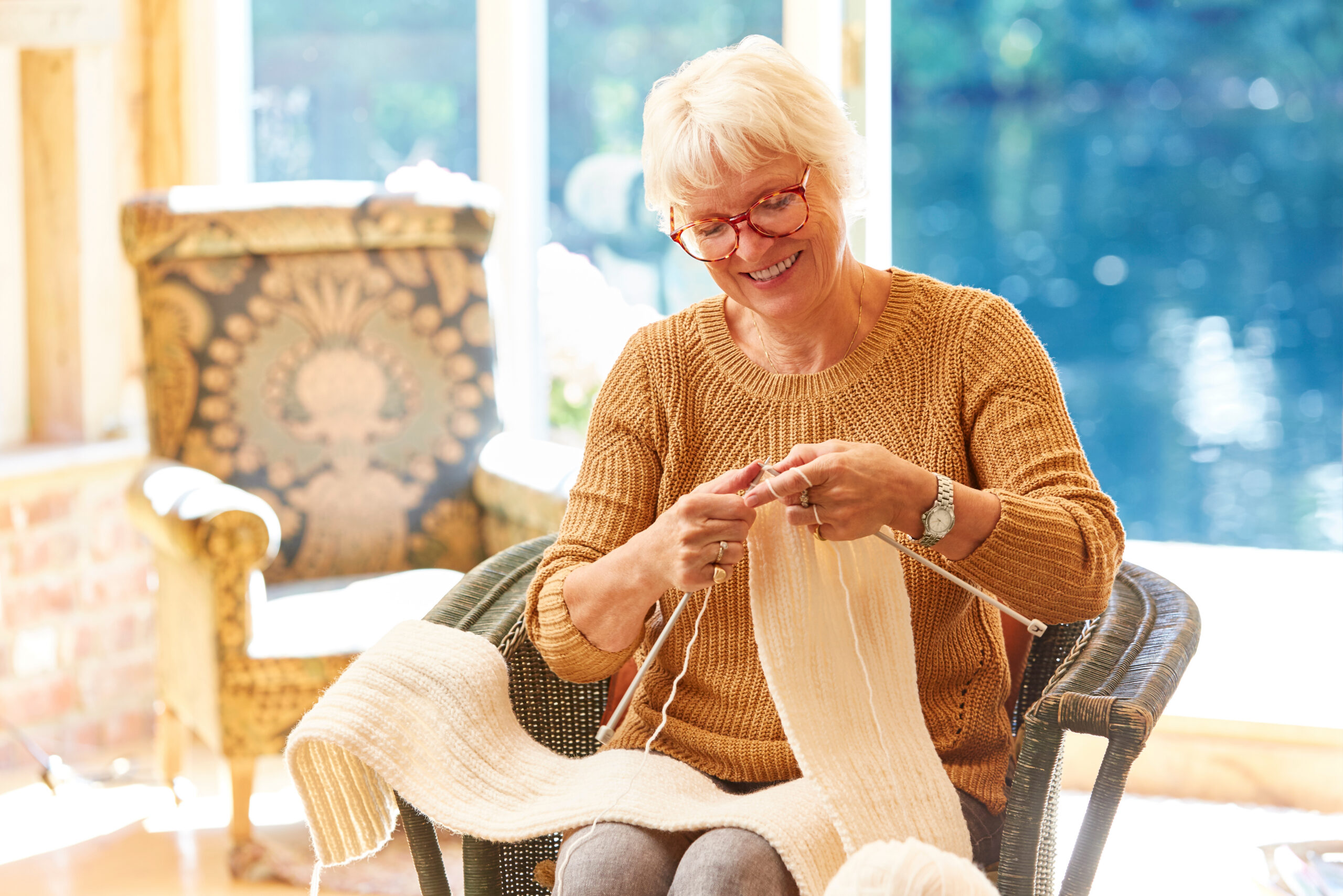 White older woman knitting while sun is shinning through window.
