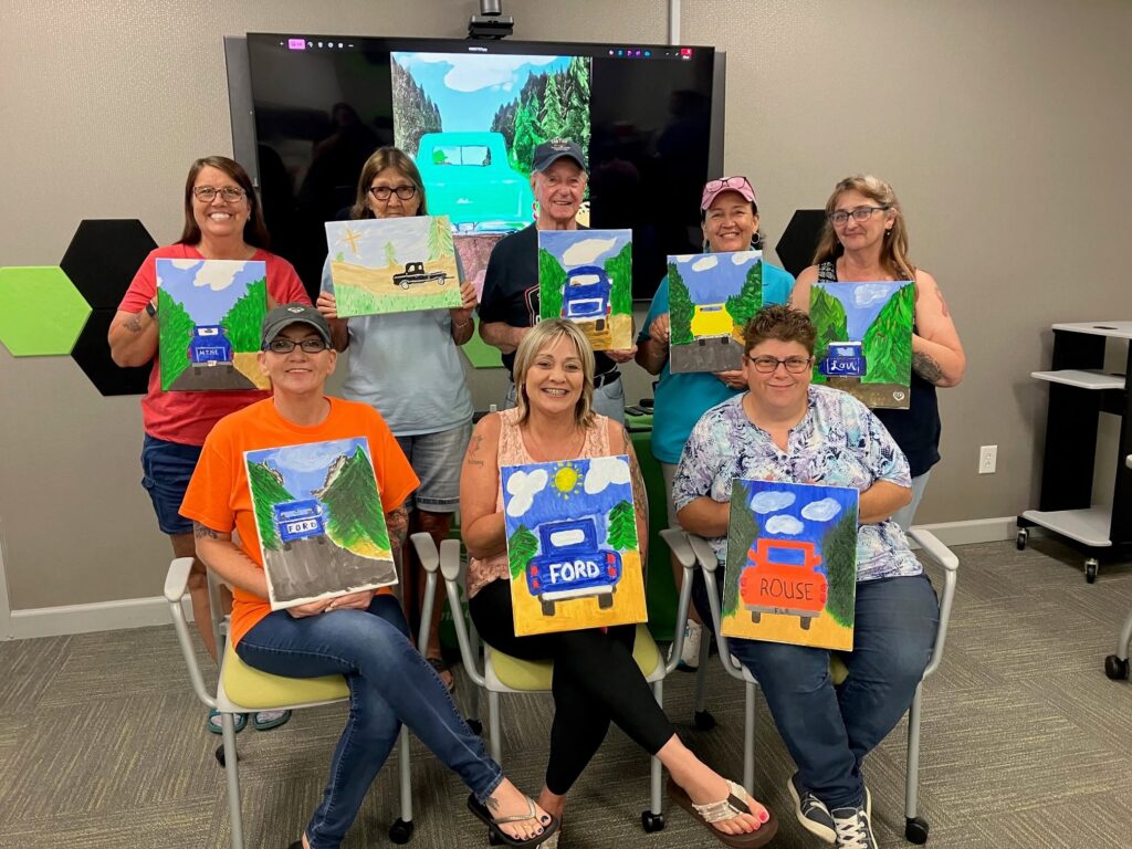 Group of art students holding up paintings and smiling at camera