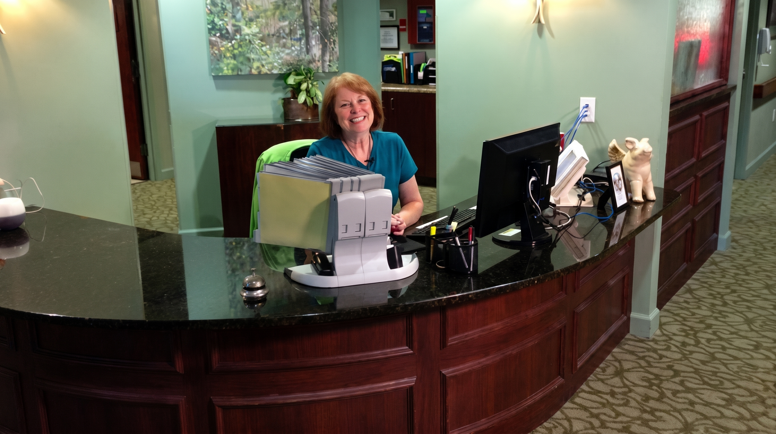 Woman smiling at front desk, sitting behind a computer