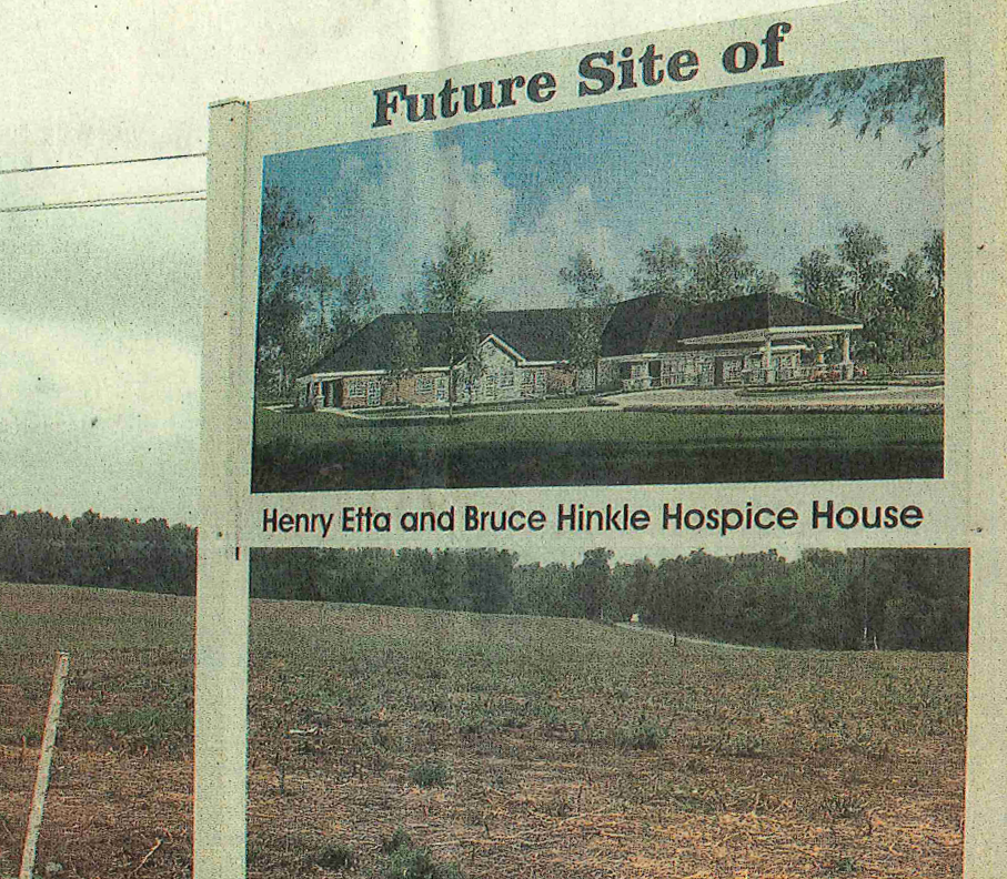 Newspaper picture of a sign in a field that says "Future Site of Henry Etta and Bruce Hinkle Hospice House" with a picture of the Hospice House architectural rendering.